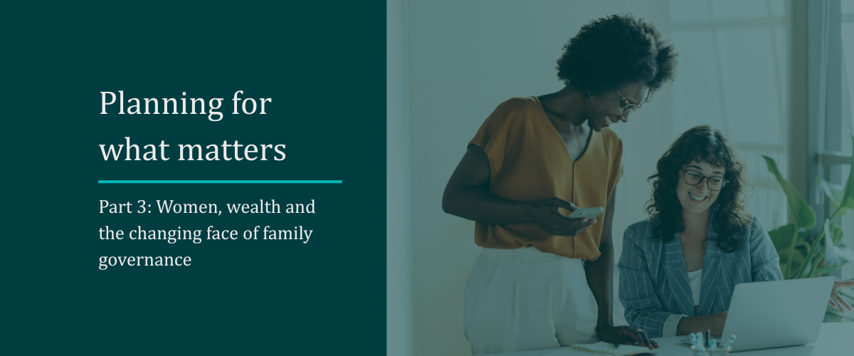 two women stand over laptop in professional setting smiling